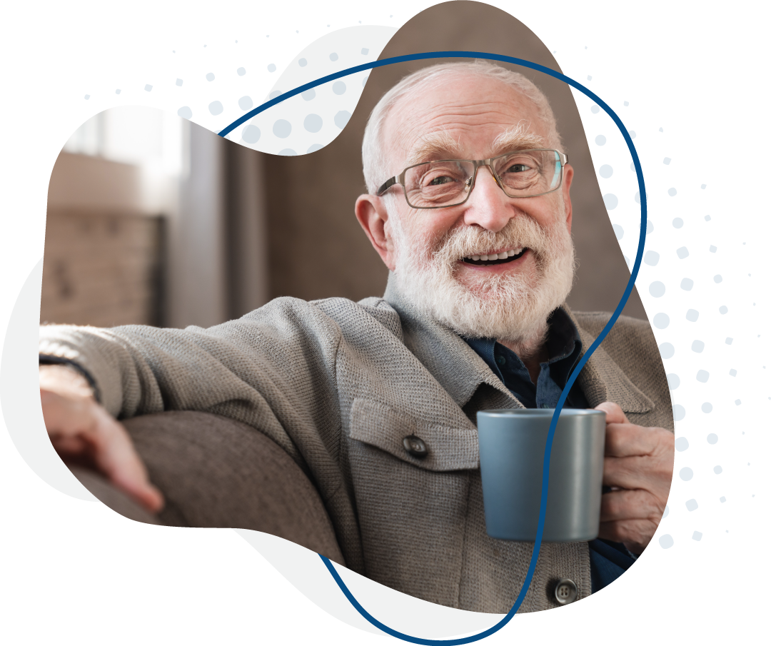 A bearded older man wearing glasses holds a coffee cup, exuding a relaxed and friendly demeanor.